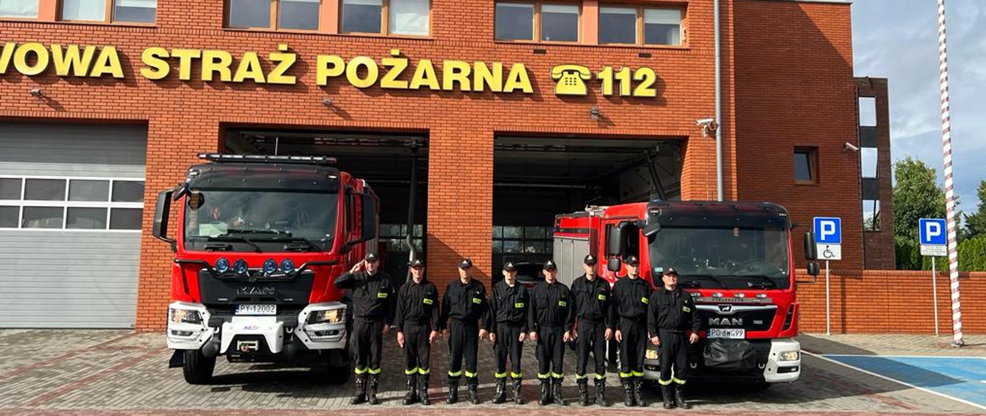 strażacy stoją pomiędzy samochodami jeden z nich oddaje honor.