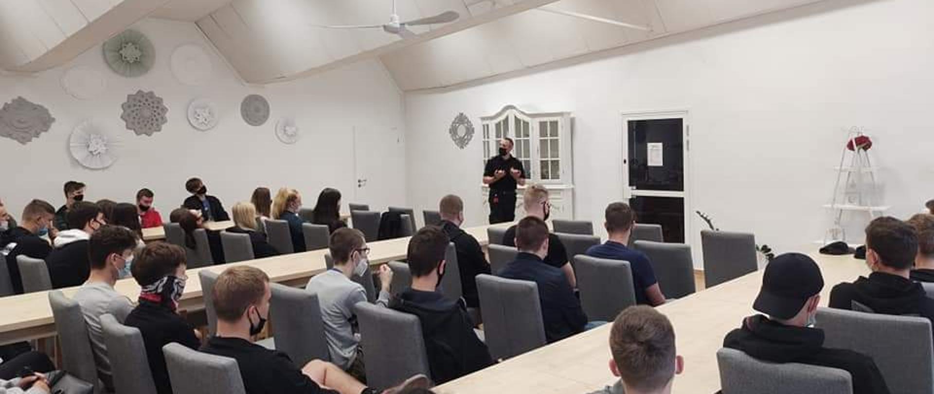 Sala wykładowa na na której uczniowie słuchają pracownika straży pożarnej