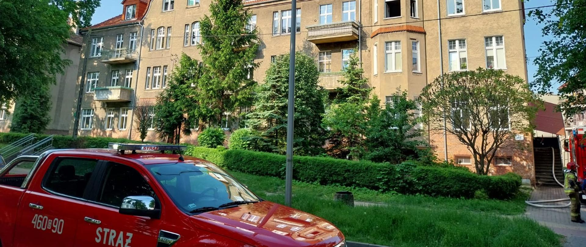 Samochód operacyjny na tle budynku wielorodzinnego, w którym doszło do pożaru.