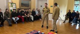 Strażacy z JRG PSP Czarnków podczas pokazu udzielania pierwszej pomocy – w sali szkoły zebrani uczniowie obserwują instruktaż przy fantomie.