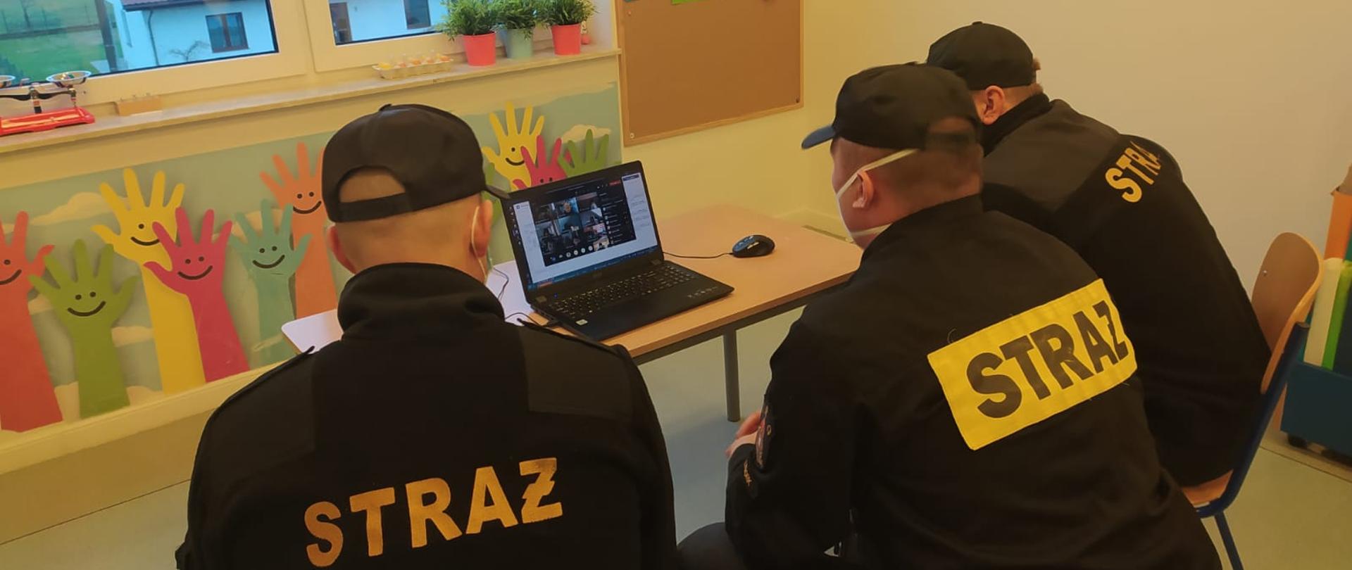 Strażacy prowadzą zajęcia dla dzieci korzystając z komputera w formie wideokonferencji.
