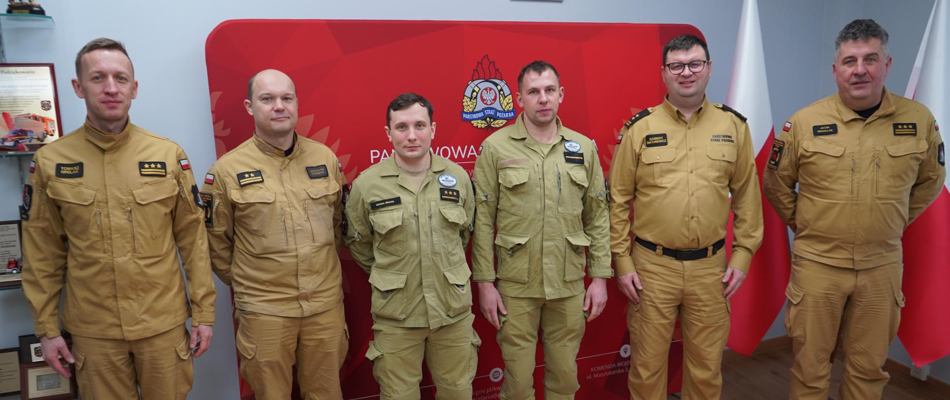 Zdjęcie przedstawia funkcjonariuszy PSP, komendantów, dowódcę oraz wyróżnionych strażaków. Wszyscy stoją ustawieni w szeregu.