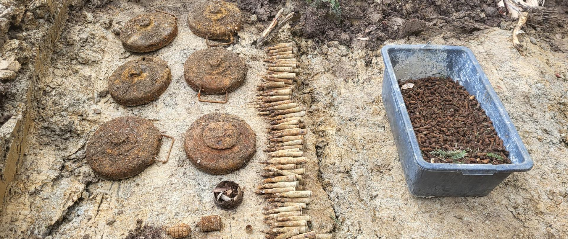Wykopane z ziemi zardzewiałe miny przeciwpancerne, pociski i łuski amunicji ułożone obok plastikowej skrzynki pełnej łusek.