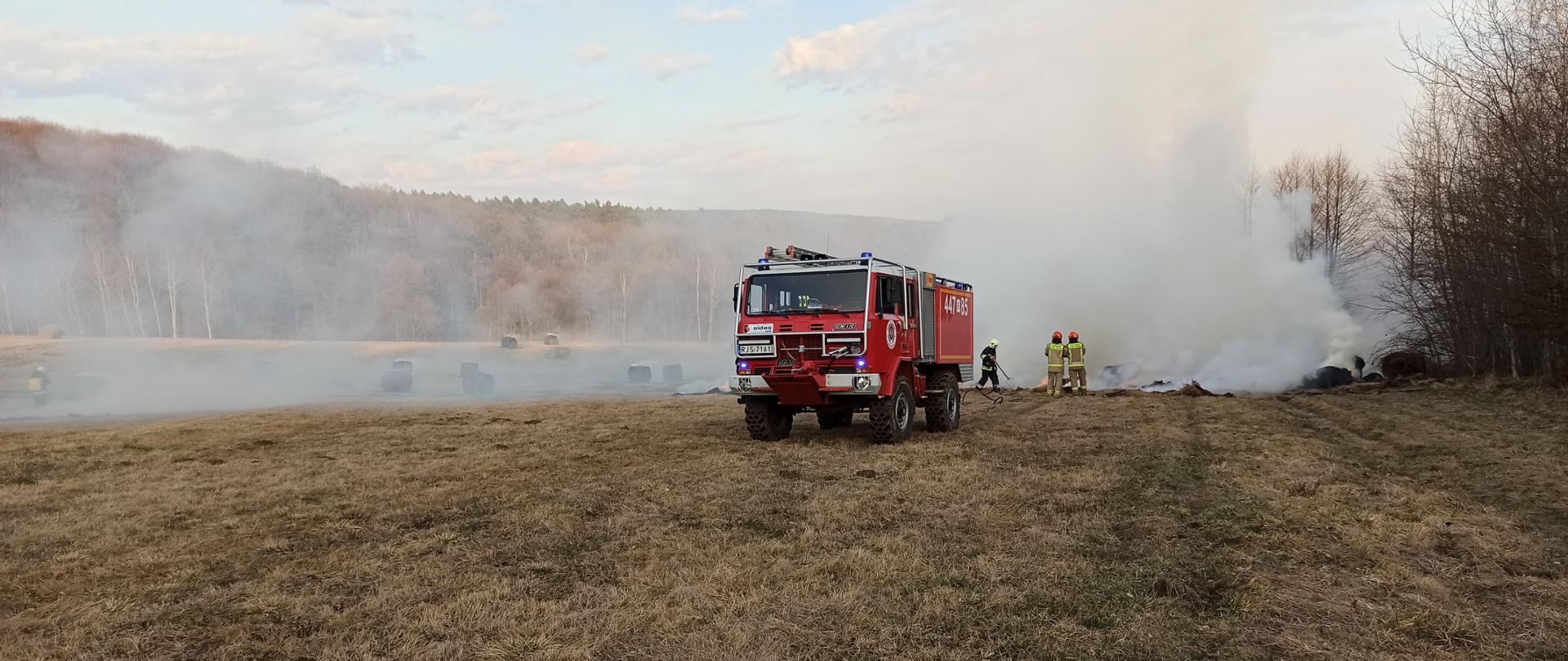 Na zdjęciu wóz strażacki oraz strażacy z OSP gaszący pożar bali siana oraz traw