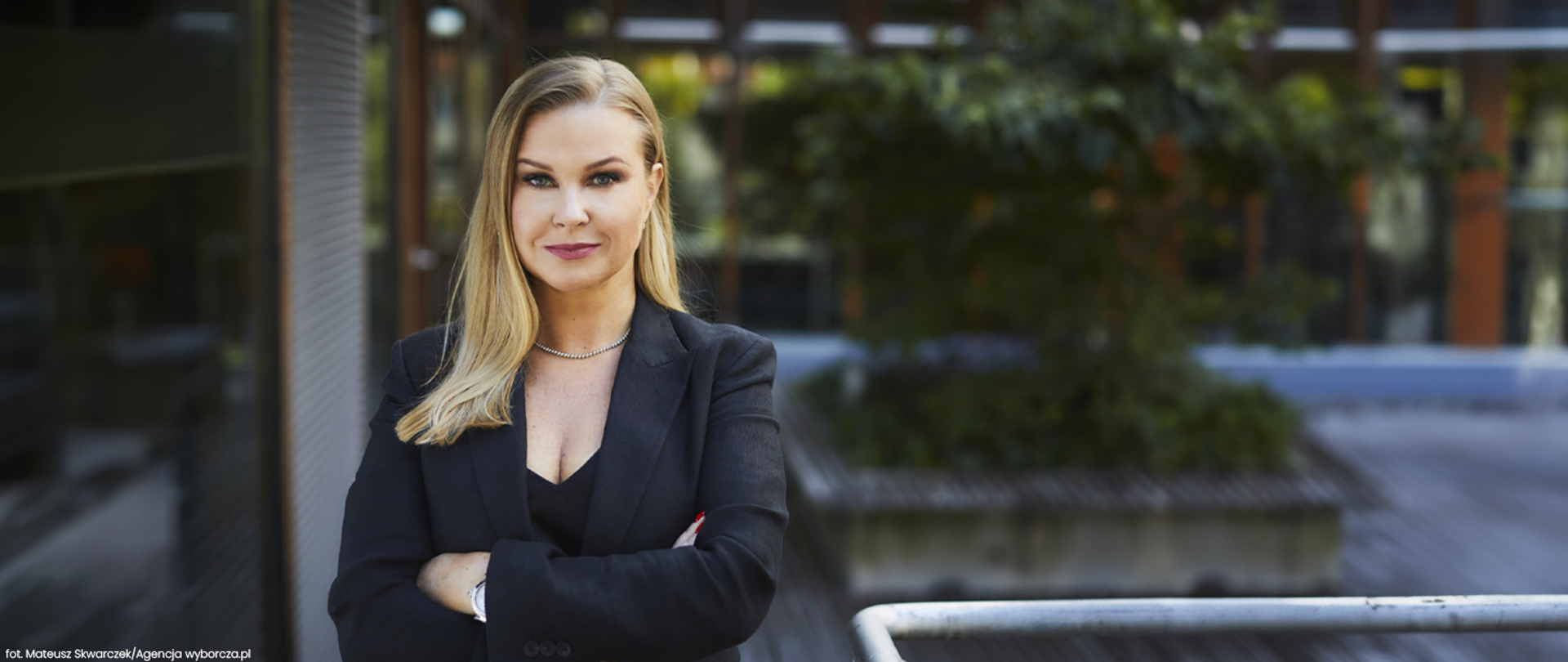 Na pierwszym planie stoi kobieta. Tło jest rozmyte. 