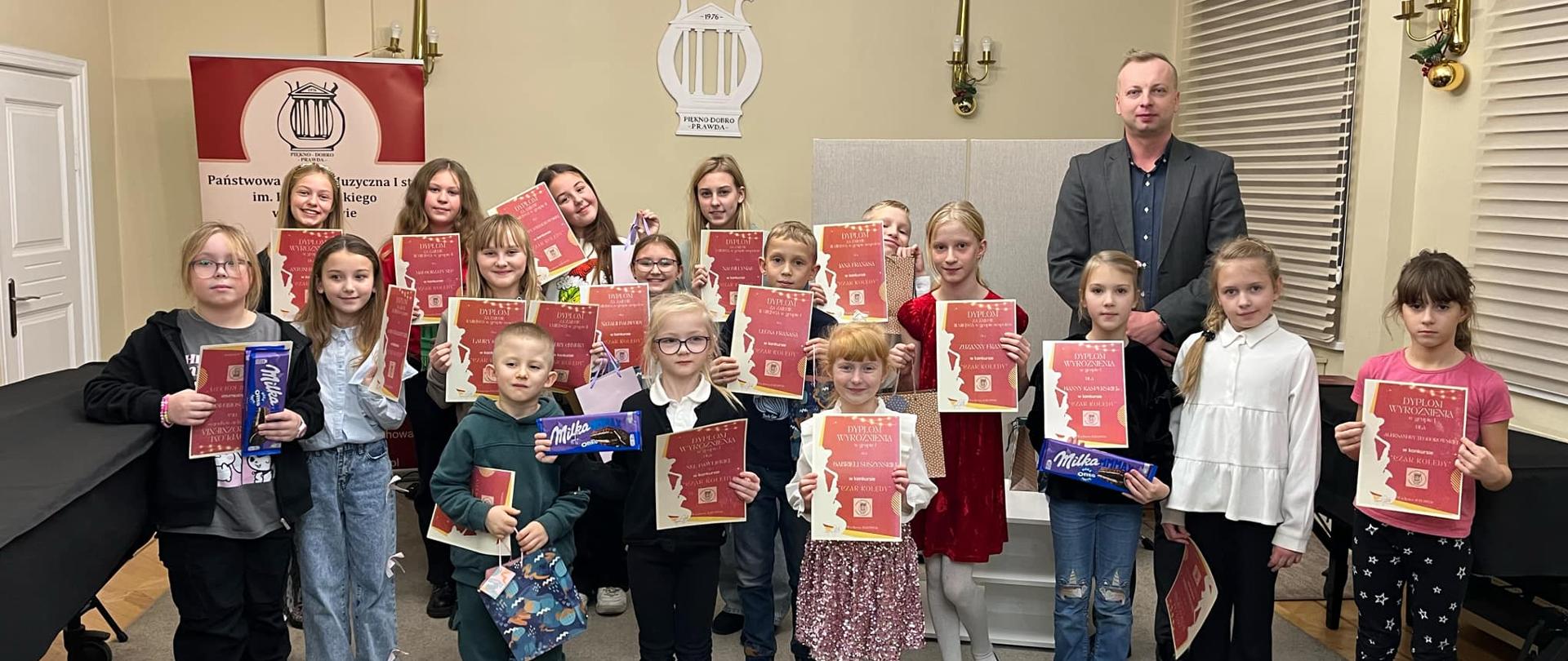 Uczniowie z dyplomami i nagrodami wraz z dyrektorem w auli szkoły.