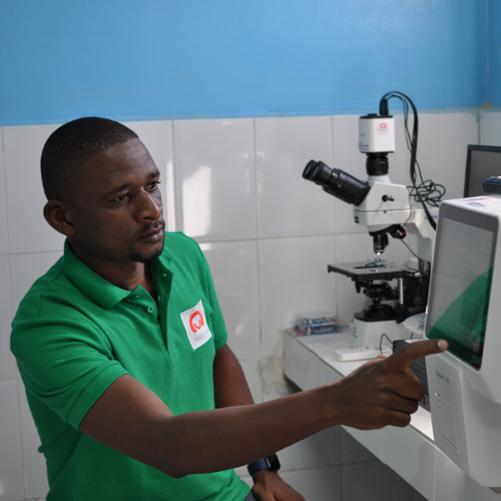 Mężczyzna w zielonej koszulce polo z logo polskiej pomocy obsługuje nowoczesną aparaturę laboratoryjną