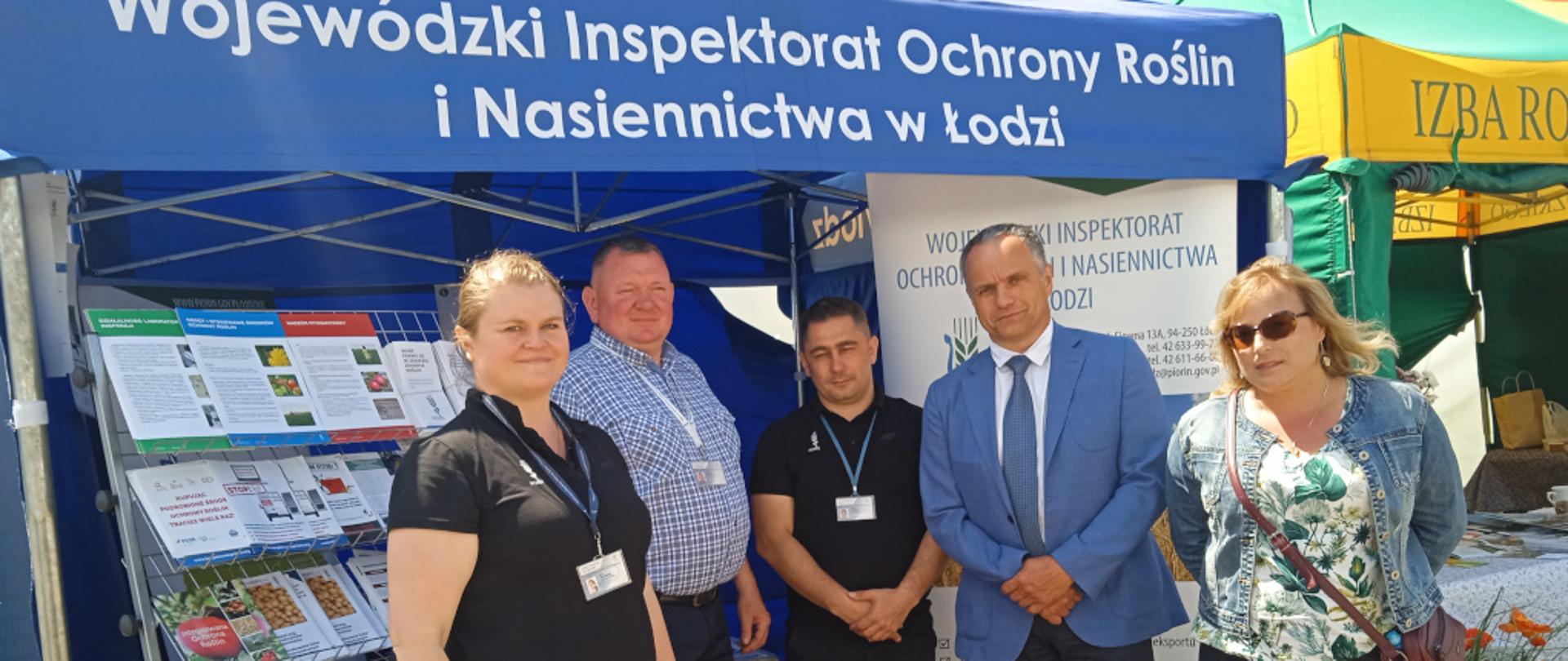 Pracownicy Wojewódzkiego Inspektoratu Ochrony Roślin i Nasiennictwa w Łodzi i Oddziału w Brzezinach pod niebieskim namiotem. Obok rozłożone ulotki i banery