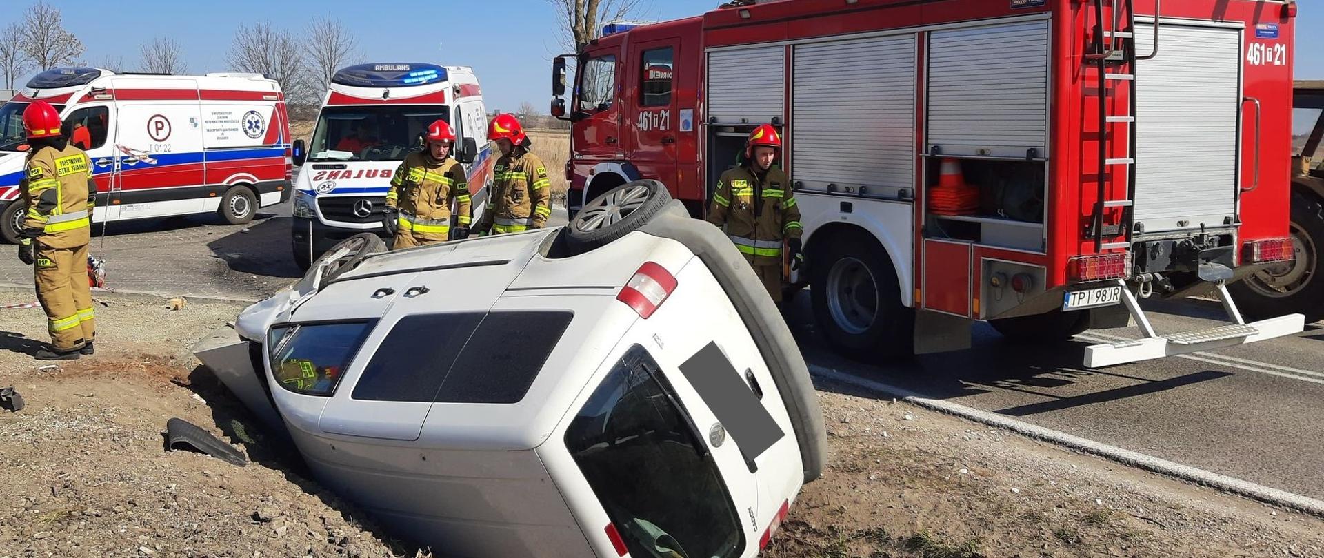 Zdjęcie przedstawia strażaków prowadzących działania w obrębie wraku pojazdu oraz wozy bojowe JOP i pojazdy PRM.