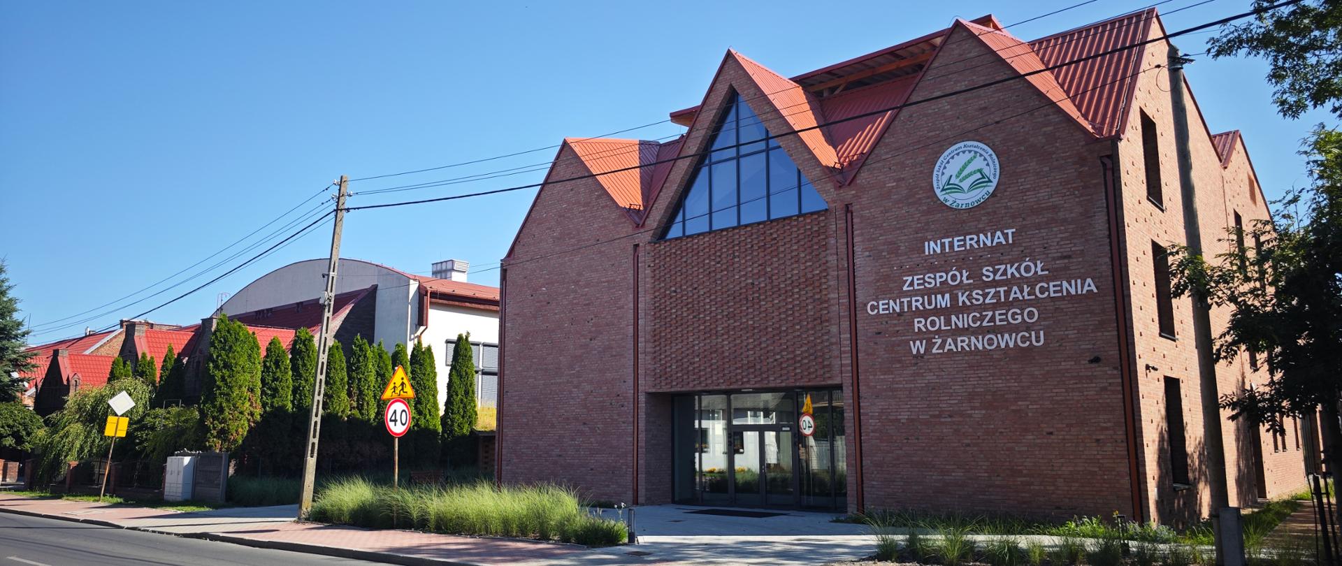 Budynek internatu Zespołu Szkół Centrum Kształcenia Rolniczego w Żarnowcu, w oddali krzewy i budynki