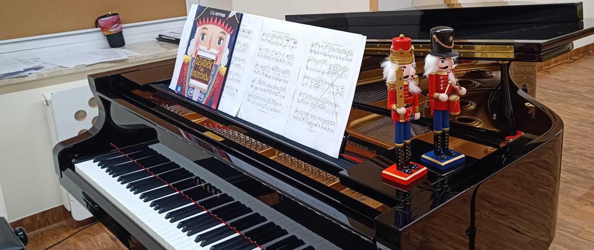 Fragment fortepianu, na pulpicie nuty i okładka książki "Dziadek do orzechów, na skrzyni fortepianu stoją dwie drewniane figurki przedstawiające żołnierzy.