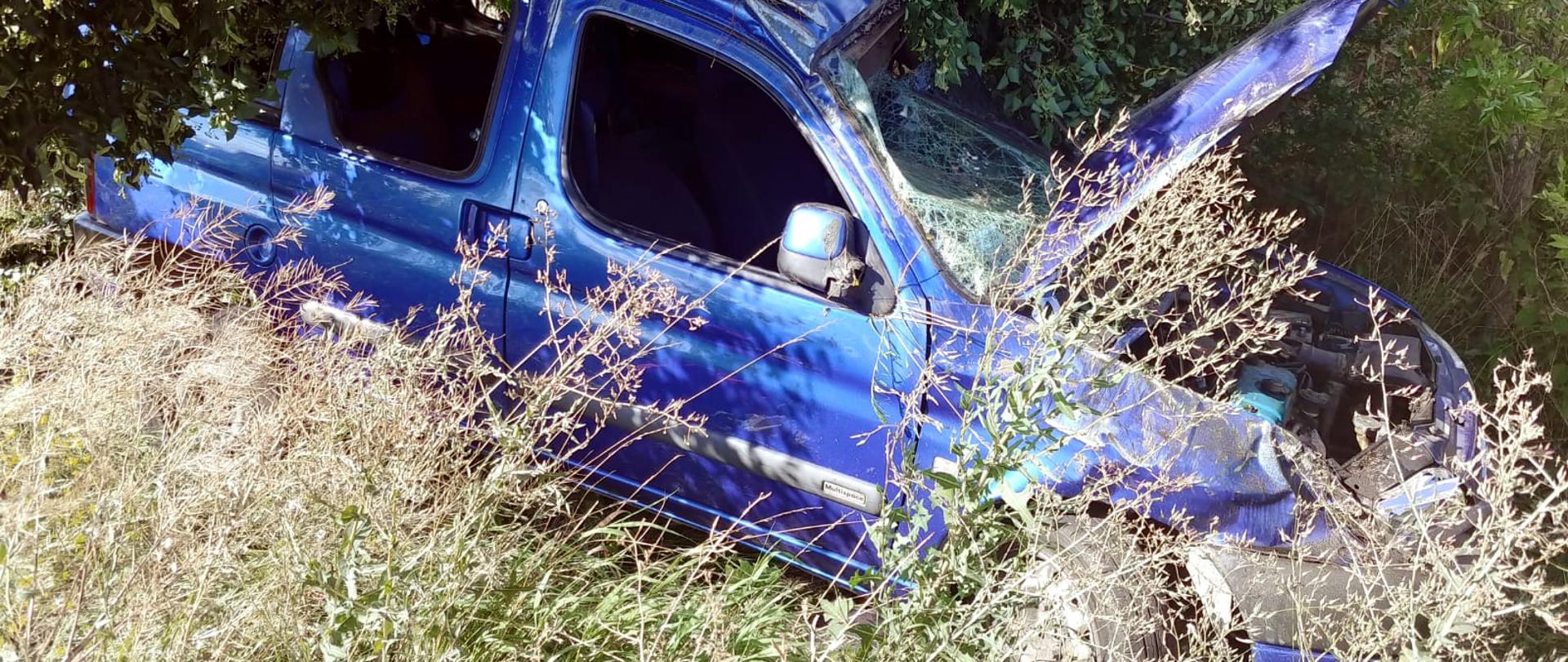 zniszczony samochód stoi pod drzewem, otwarta maska powybijane szyby