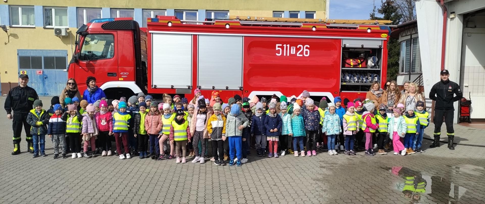 Plac wewnętrzny KP PSP, grupowe zdjęcie uczestników wycieczki na tle samochodu ratowniczo-gaśniczego.