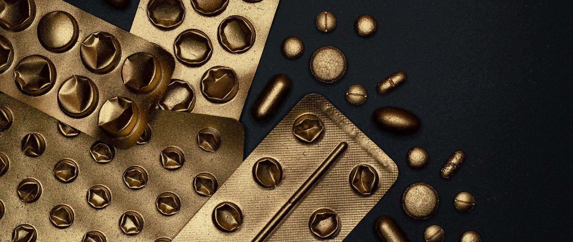 złote blistry po tabletkach na czarnym tle.