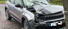 Srebrny samochód uderzył w drzewo ma uszkodzoną maską oraz przód pojazdu
