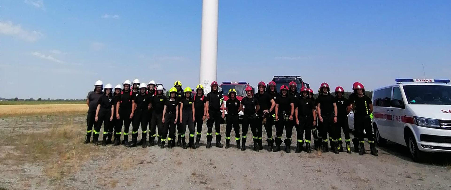 Zdjęcie przedstawia uczestników szkolenia stojących pod turbiną wiatrową.