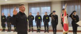 Na zdjęciu widoczny strażak w postawie do ślubowania. W tle strażacy uczestniczący w ceremonii oraz sztandar Komendy Powiatowej PSP.