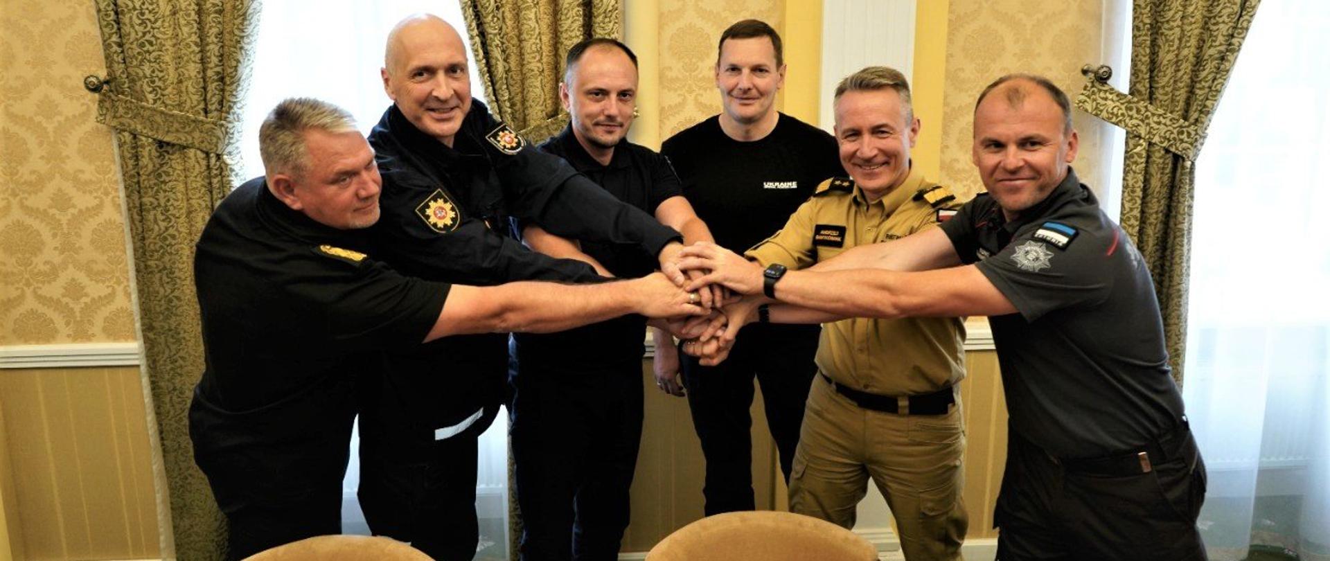 Na zdjęciu widać jak szefowie służb ratowniczych z Polski, Litwy, Łotwy i Estonii w Ukrainie nakładają swoje ręce na siebie