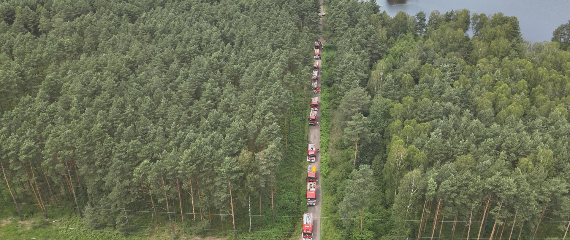 Zdjęcie z dronu.. Na drodze leśnej stoi rząd samochodów strażackich.