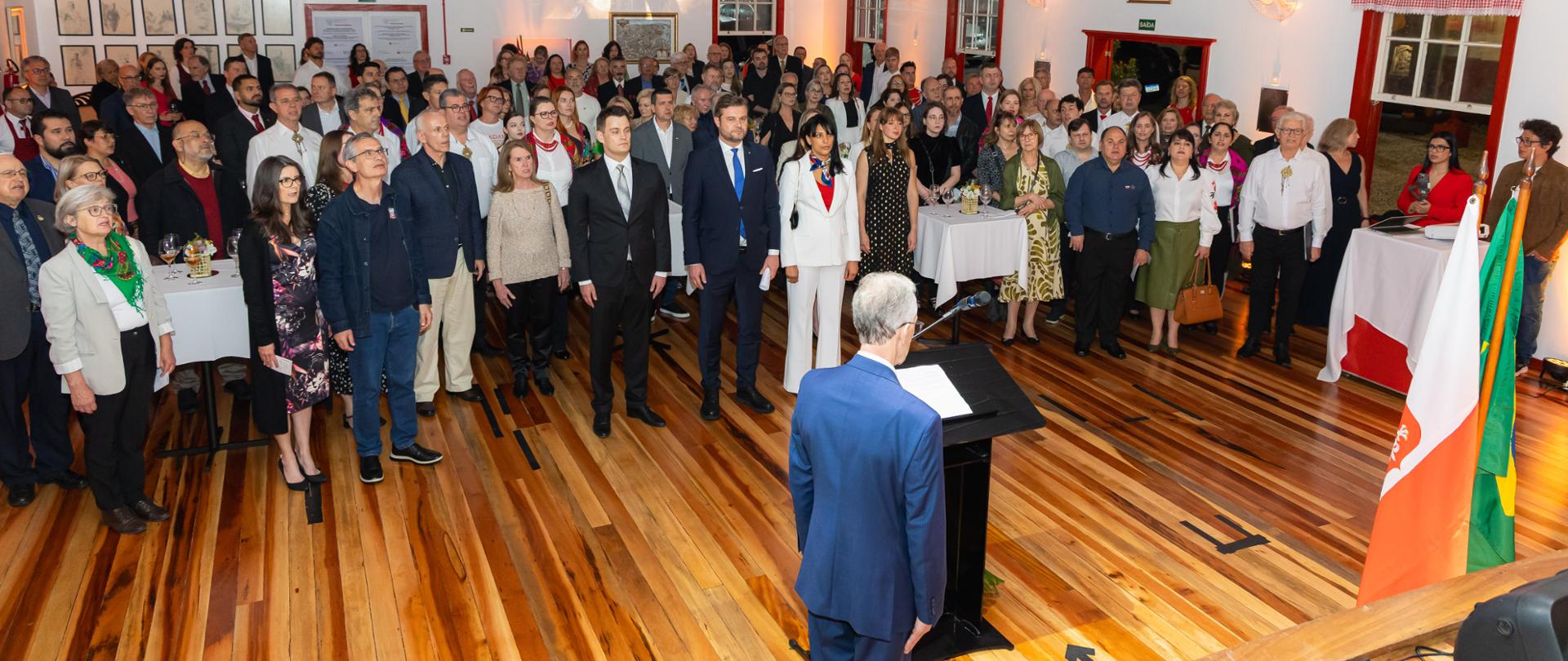 Numero público em pé, cantando o hino nacional da República da Polônia