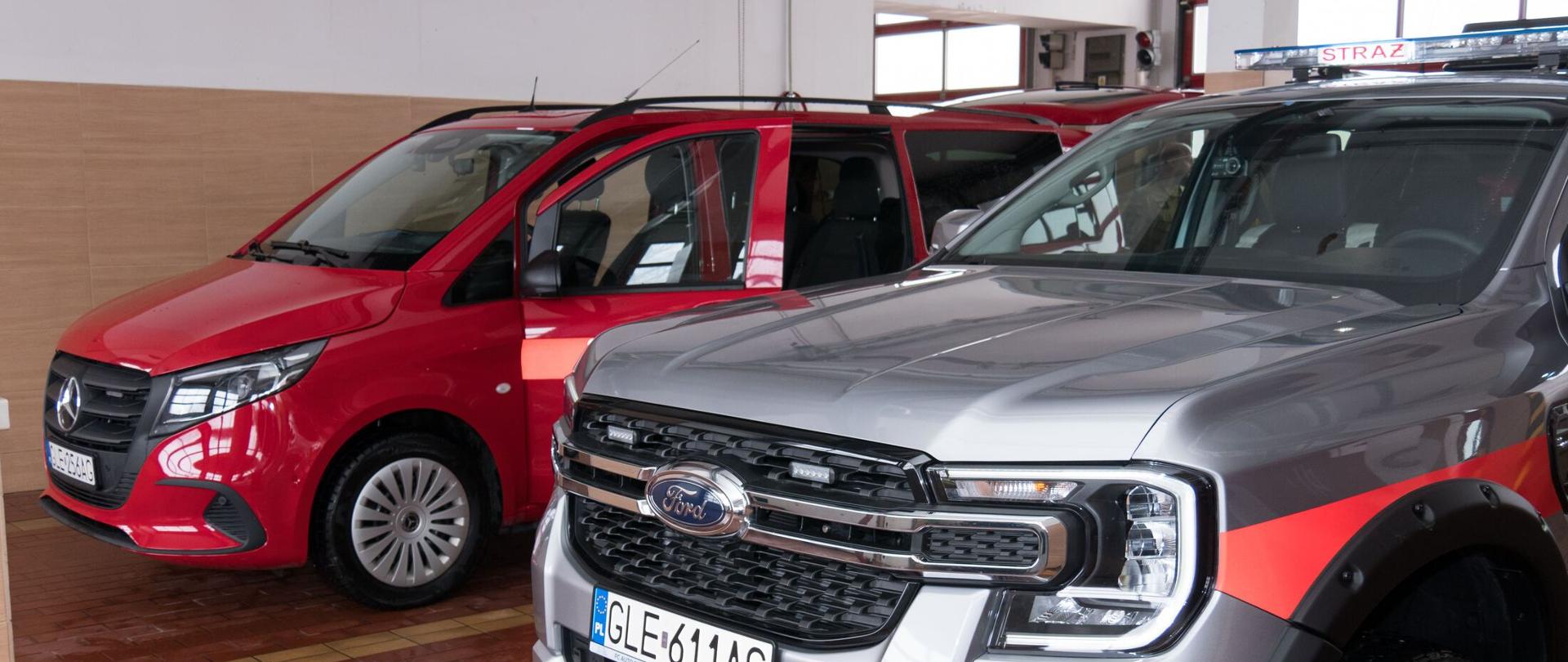W garażu komendy obok siebie stoją dwa samochody. Od lewej strony samochód Mikrobus Mercedes Vito w kolorze czerwonym, po prawej stronie samochód specjalny rozpoznawczo-ratowniczy Ford Ranger Limited koloru szarego.