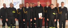 Zdjęcie przedstawia funkcjonariuszy PSP oraz pracowników cywilnych z nowo przyjętym strażakiem