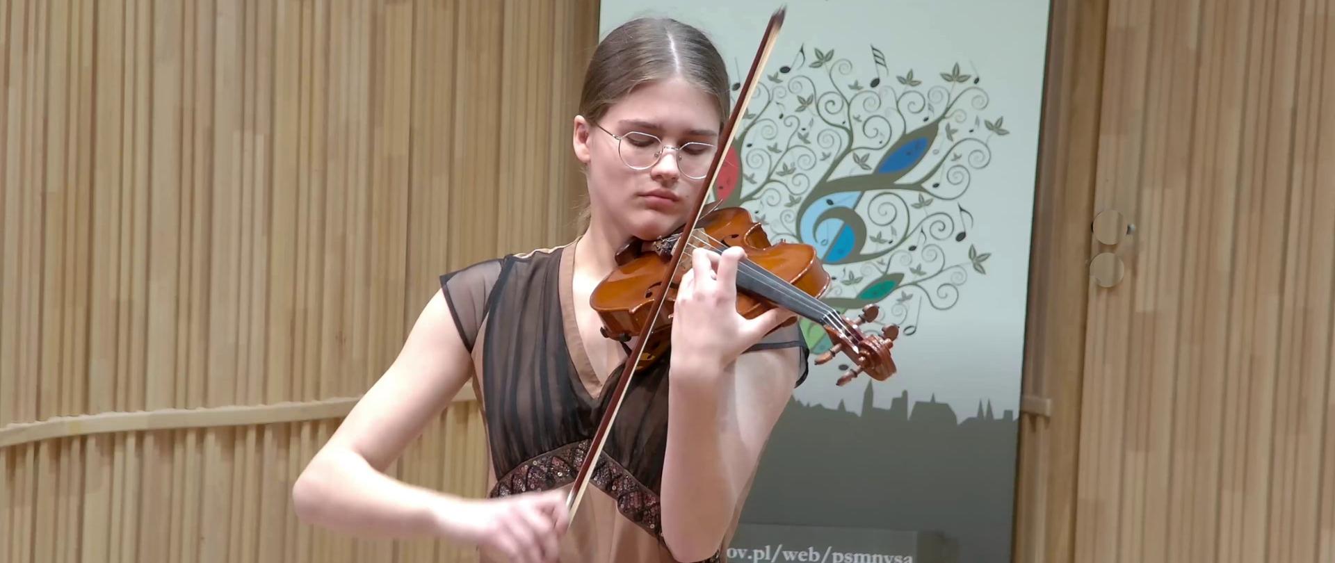 Zdjęcie. Skrzypaczka podczas koncertu na estradzie Sali Koncertowej PSM I i II stopnia w Nysie. W tle widać baner PSM Nysa.
