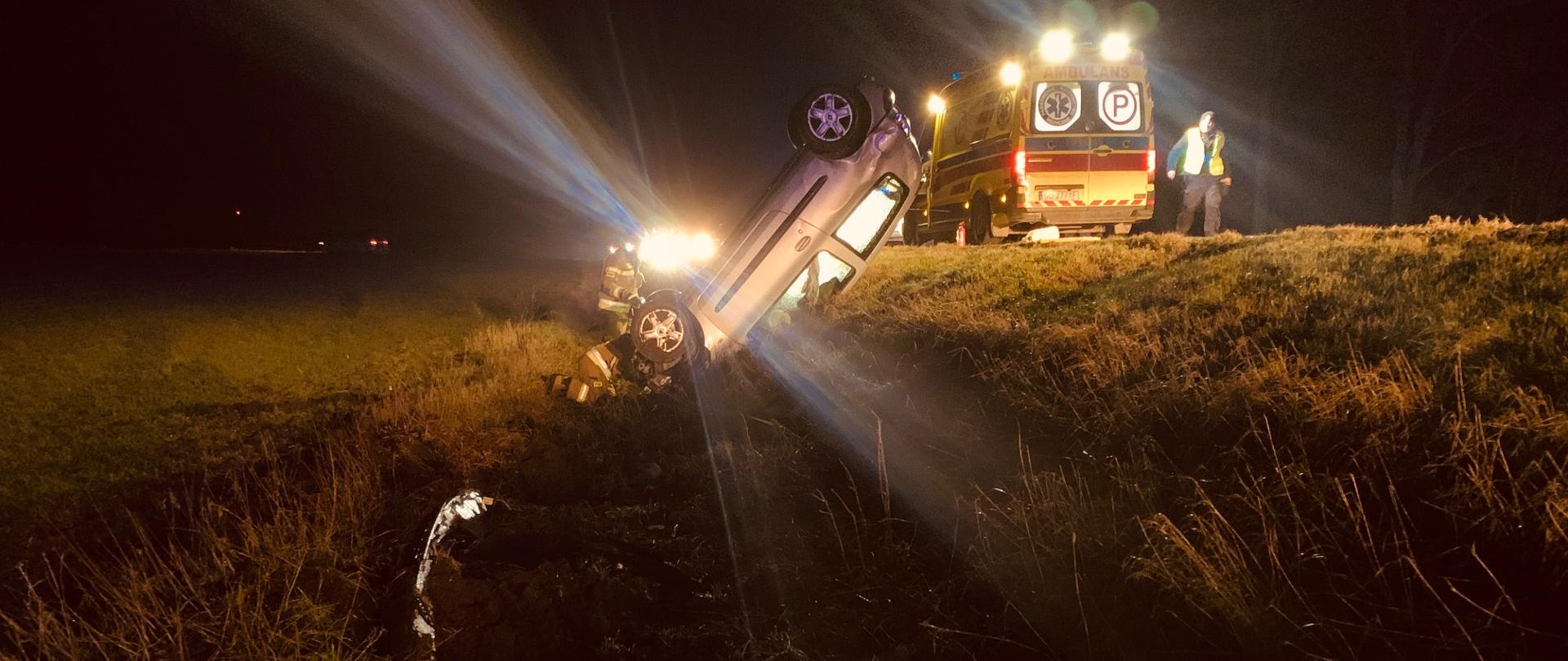 Samochód osobowy w przydrożnym rowie. Na drodze stoi karetka pogotowia