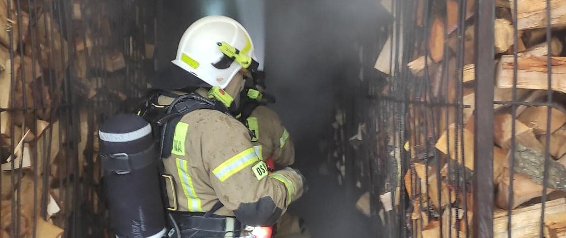 Zdjęcie przedstawia dwóch strażaków z linią gaśniczą przystępujących do gaszenia pożaru suszarni w Kołaczu