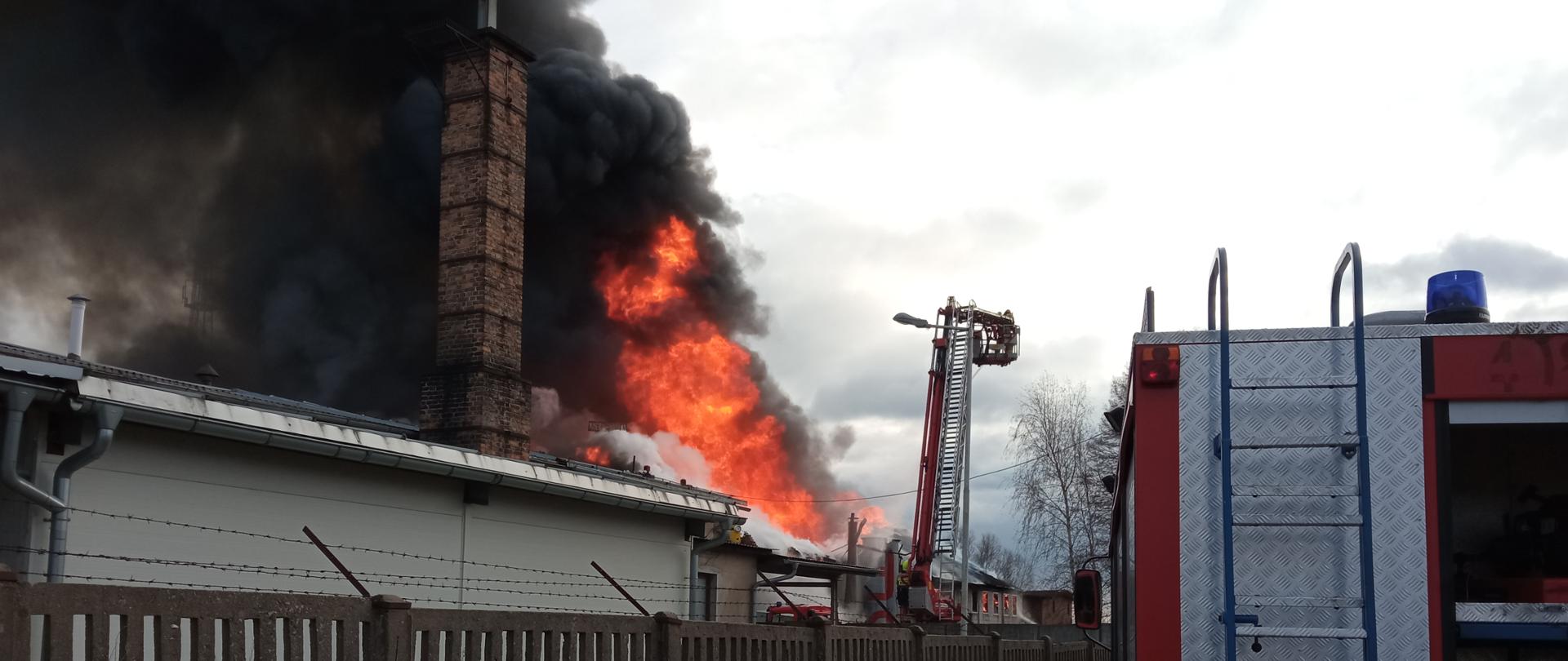 Fotografia przedstawia ujęcie wczesnej fazy działań. Widoczny pożar budynku oraz rozstawiony podnośnik hyrauliczny.