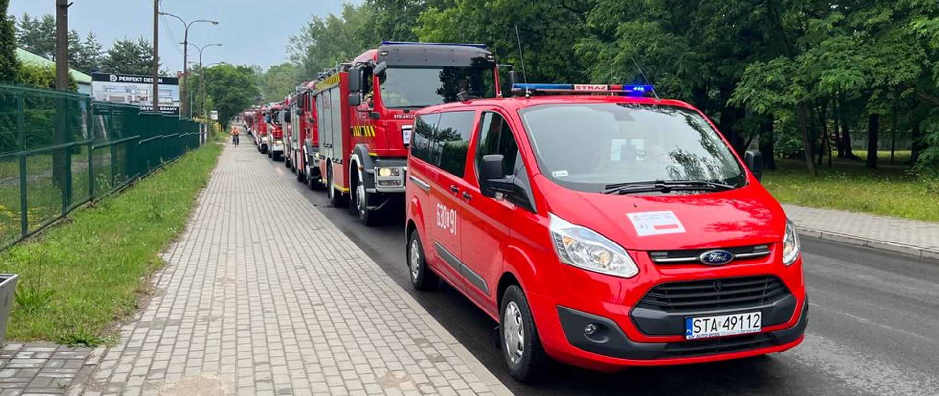 Na ulicy stoi kolumna pojazdów strażackich w kolorach czerwonych.