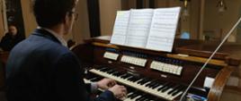 Zdjęcie przedstawia grającego organistę, widoczne nuty, kontuar organów