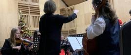 Na scenie zasiadają młodzi muzycy, przed nimi stoi dyrygentka. Widać dziewczęta grające na skrzypcach, wiolonczeli.