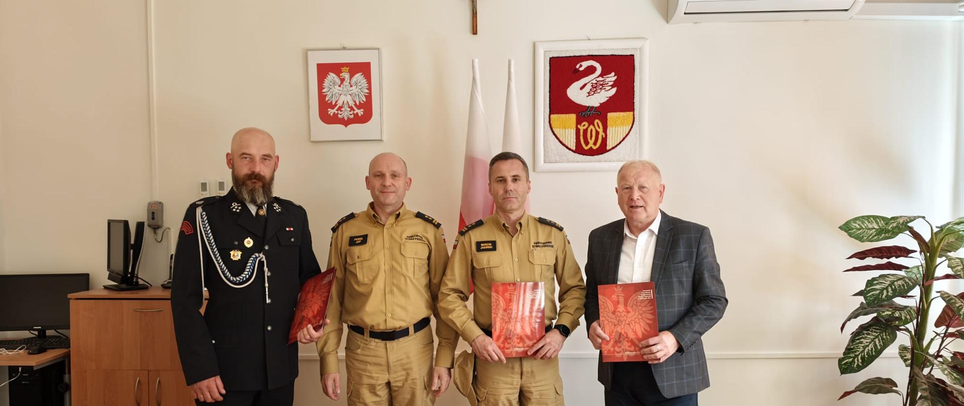 Na zdjęciu widoczny Komendant Powiatowy Państwowej Staraży Pożarnej w Ostrowcu Św., Zastępca Komendanta Powiatowego Państwowej Staraży Pożarnej w Ostrowcu Św. , Wójt Gminy Waśniów oraz Prezes Ochotniczej Straży Pożarnej w Mominie trzymający porozumienia o przedłużeniu włączenia jednostki OSP Momina do KSRG.