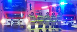 Widoczni strażacy oddający hołd na tle pojazdów gaśniczych i garaży 