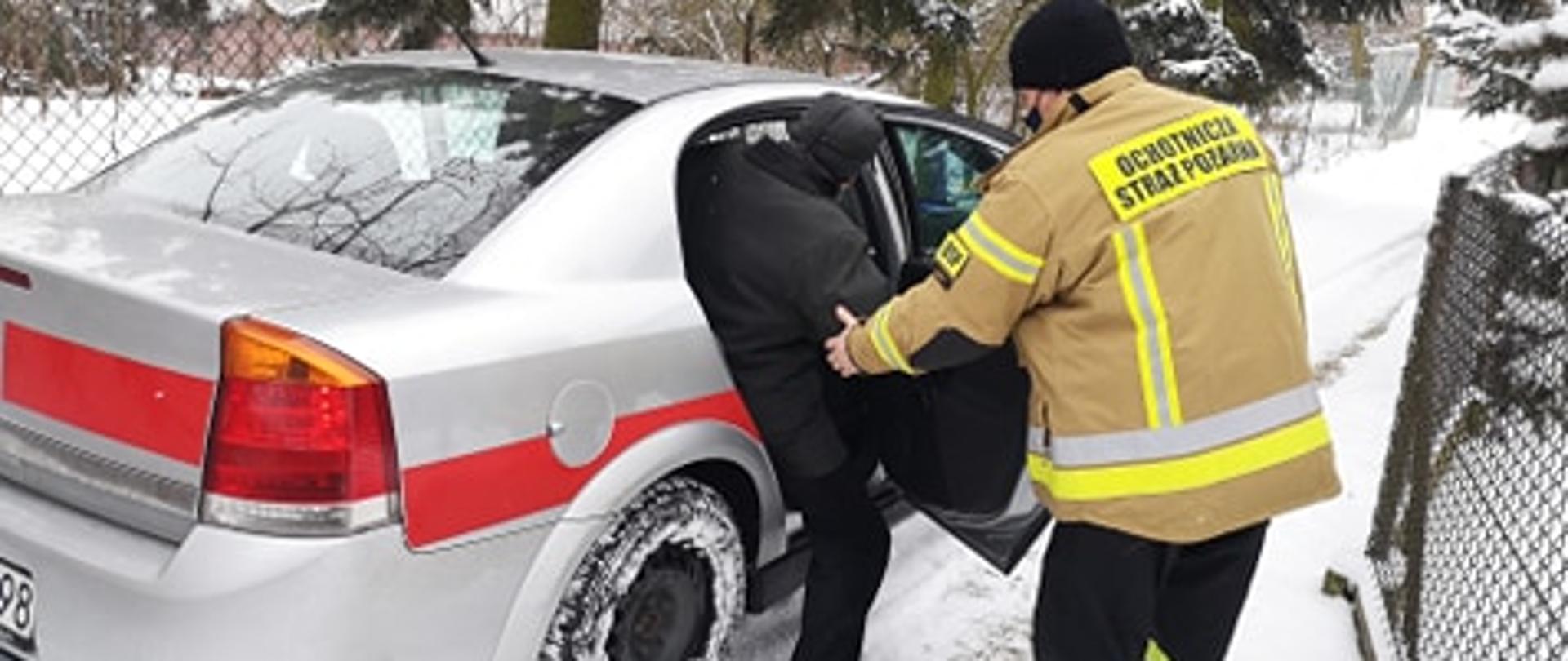 Na zdjęciu widać strażaka OSP Warta, który pomaga wysiąść z samochodu służbowego seniorowi