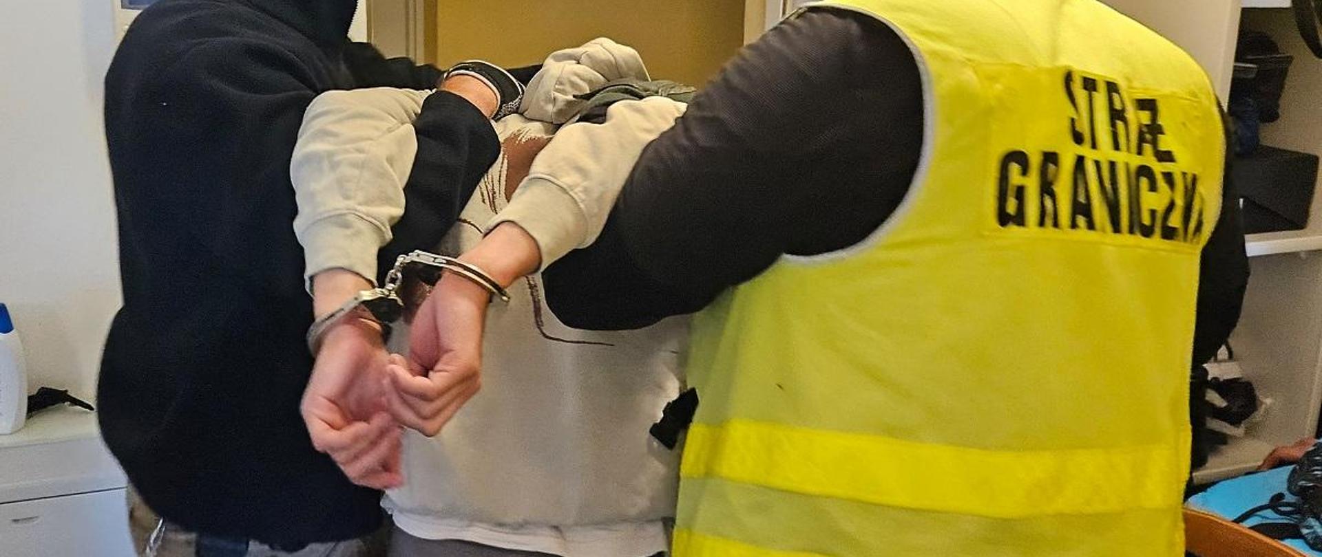 Zdjęcie przedstawia funkcjonariuszy polskiej Straży Granicznej z zatrzymanym członkiem grupy organizującej proceder nielegalnego przekraczania granicy Polski