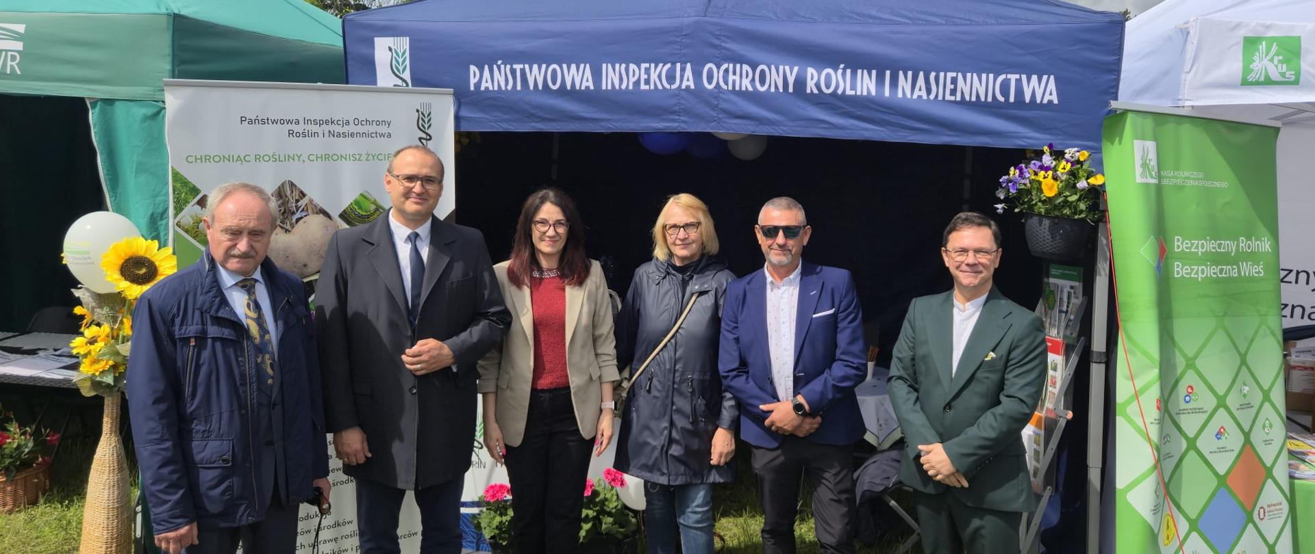 Grupa ludzi stoi przed namiotem handlowym w plenerze