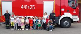 Dzieci ze strażakami na tle wozu strażackiego pozują do Zdjęcia