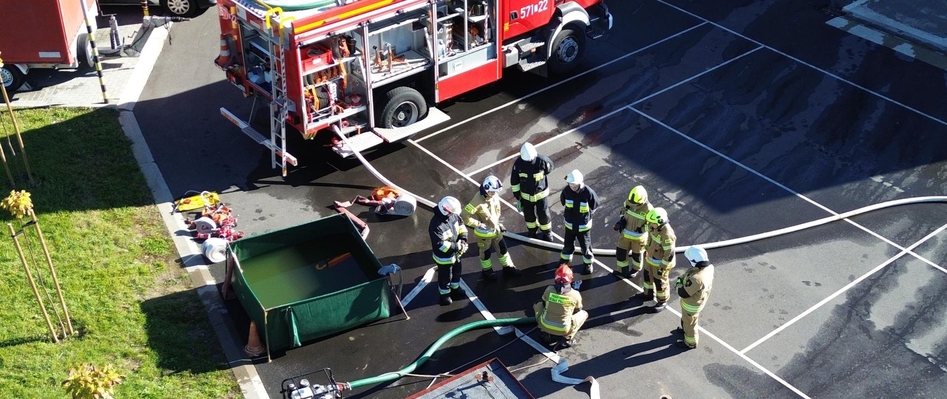 Strażacy z rozwiniętą linia gaśniczą przy zbiorniku brezentowym