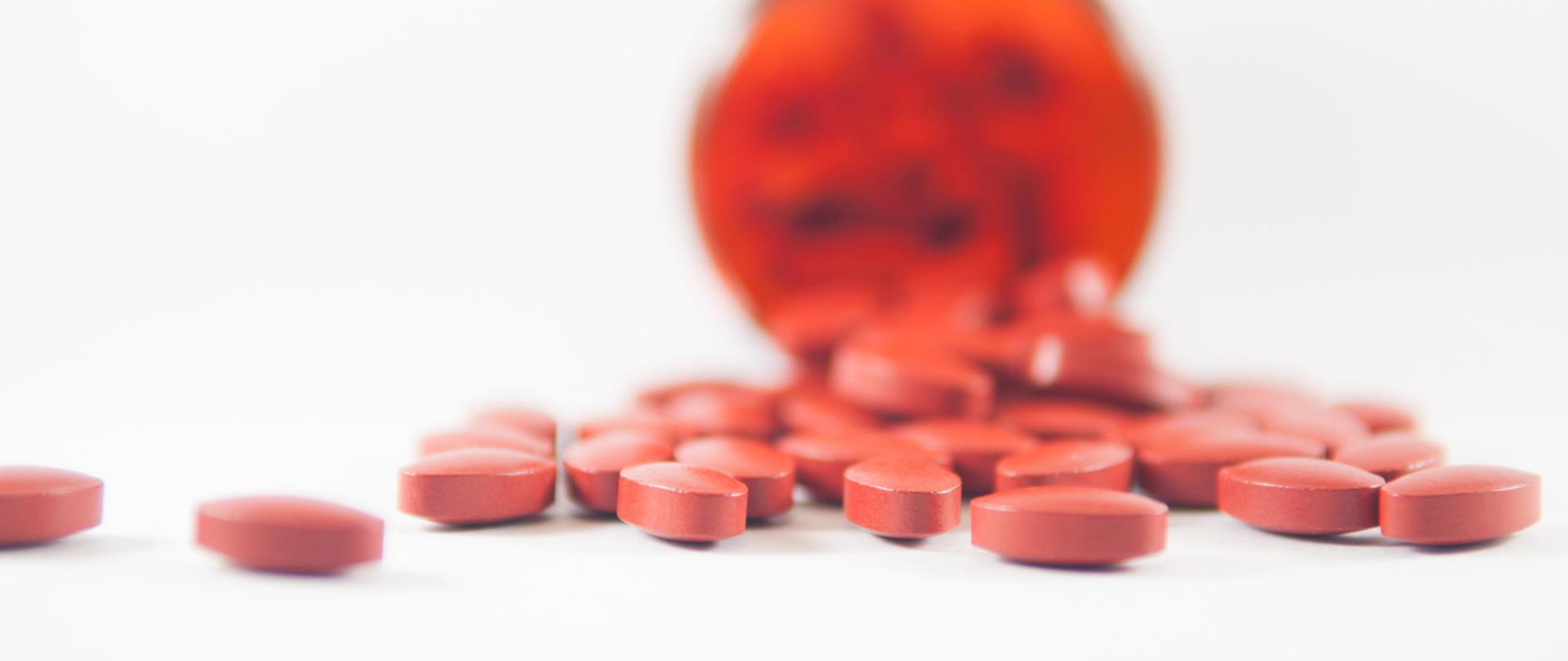 Czerwone tabletki wysypujące się z opakowania.