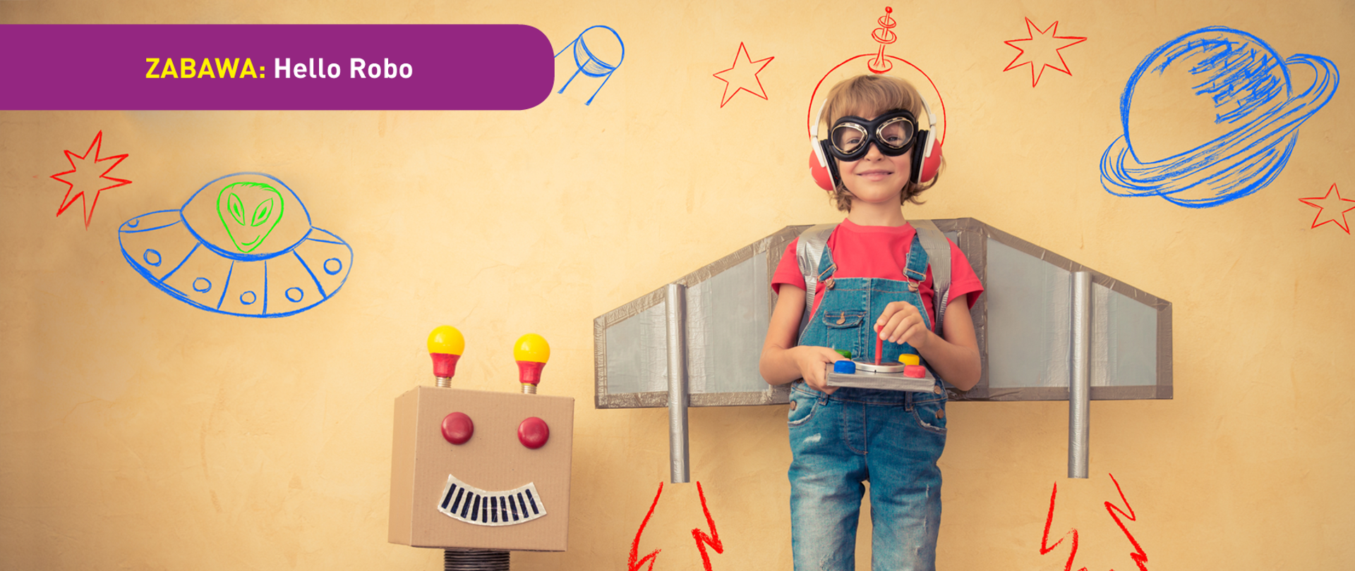 Na zdjęciu widać chłopca z przyklejoną do pleców imitacją skrzydeł samolotu. W rękach trzyma imitację pulpitu sterującego, na uszach ma słuchawki a na oczach - gogle lotnika. Obok stoi imitacja robota wykonana z kartonu. W tle widać rysunki nieba na ścianie - planety, gwiazdy, satelita, ufo. U dołu znajduje się pasek logotypów: Europejskie Fundusze Polska Cyfrowa, Ministerstwo Cyfryzacji, NASK i Unia Europejska Europejski Fundusz Rozwoju Regionalnego.