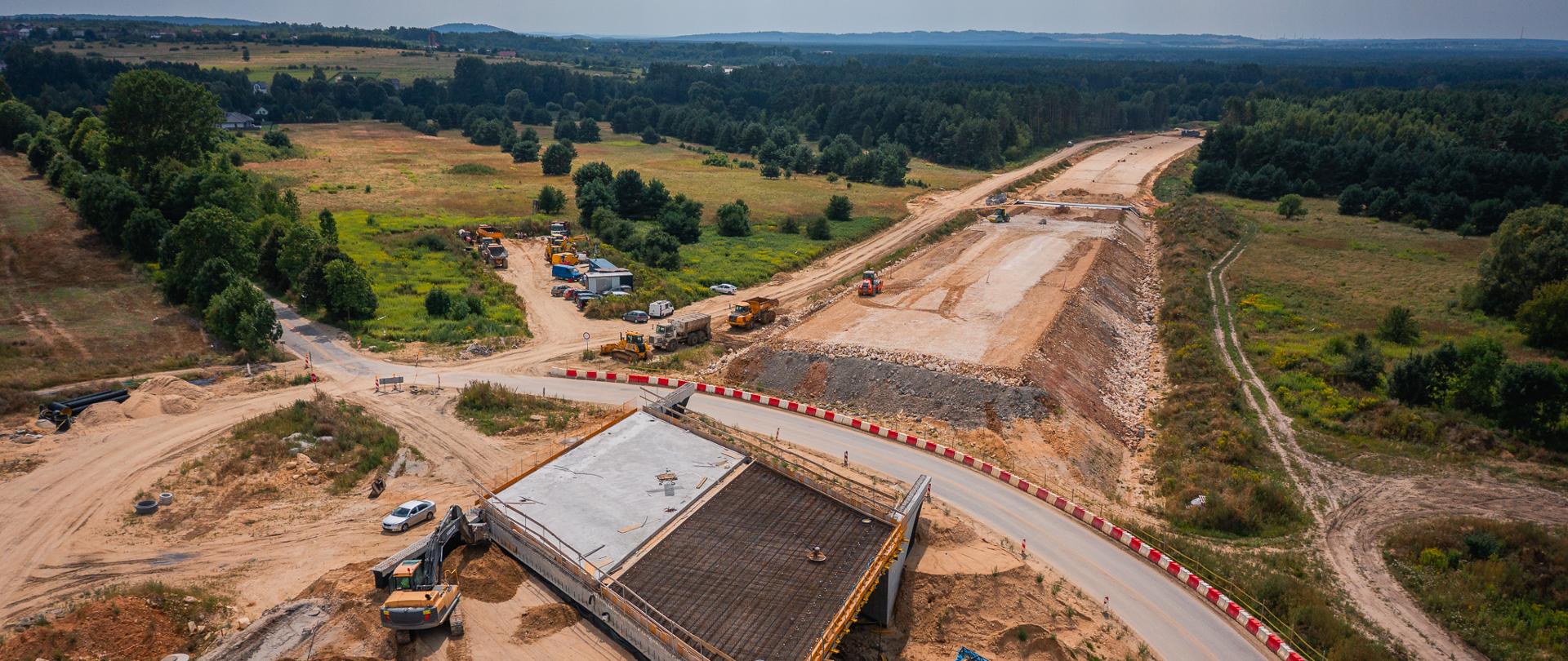 Budowa obwodnicy Zawiercia, Kroczyc i Pradeł w ciągu DK78. Widoczny ślad nowej drogi, po obu stronach las, po terenie budowy poruszają się pojazdy budowlane 