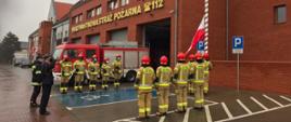 Strażacy stoją przy maszcie gzie jest podnoszona flaga