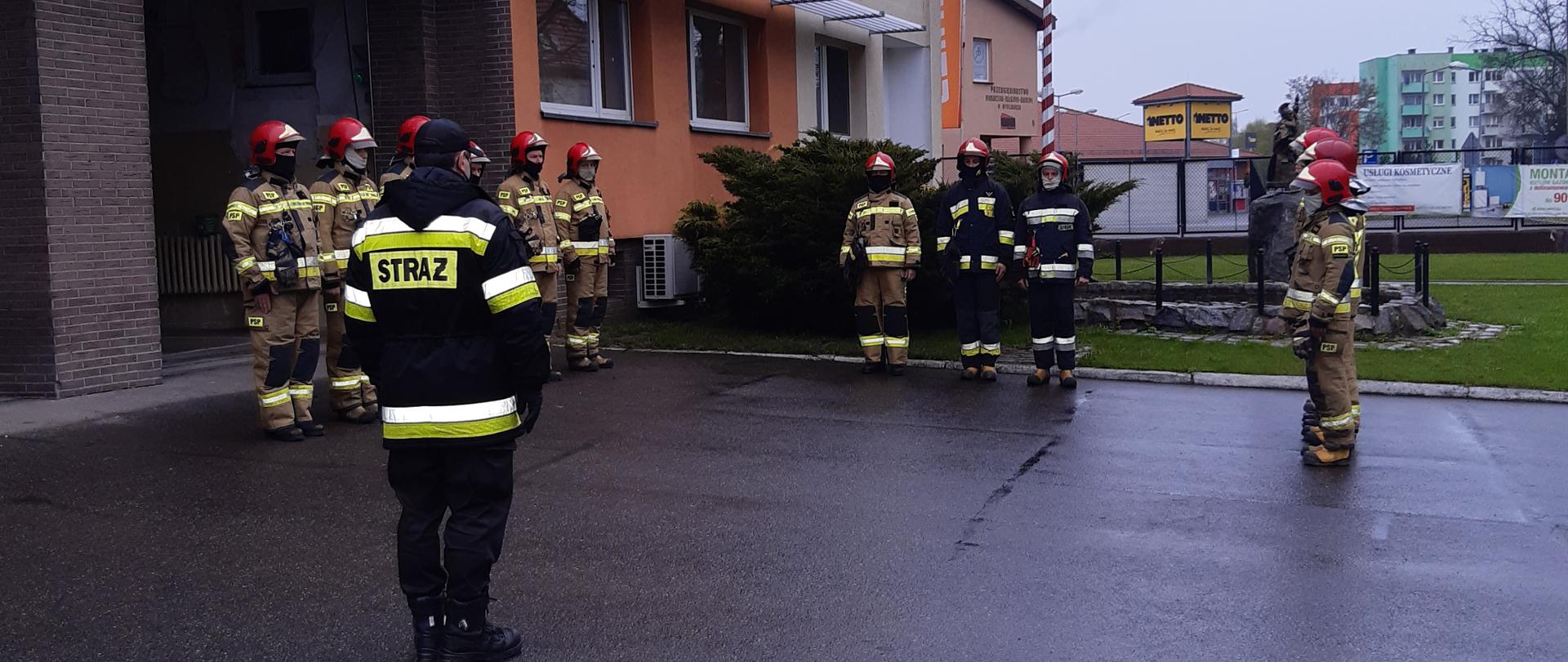Funkcjonariusze stojący w umundurowaniu bojowym na uroczystej zbiórce. Trzej z nich stoją przy maszcie i podnoszą flagę państwową.