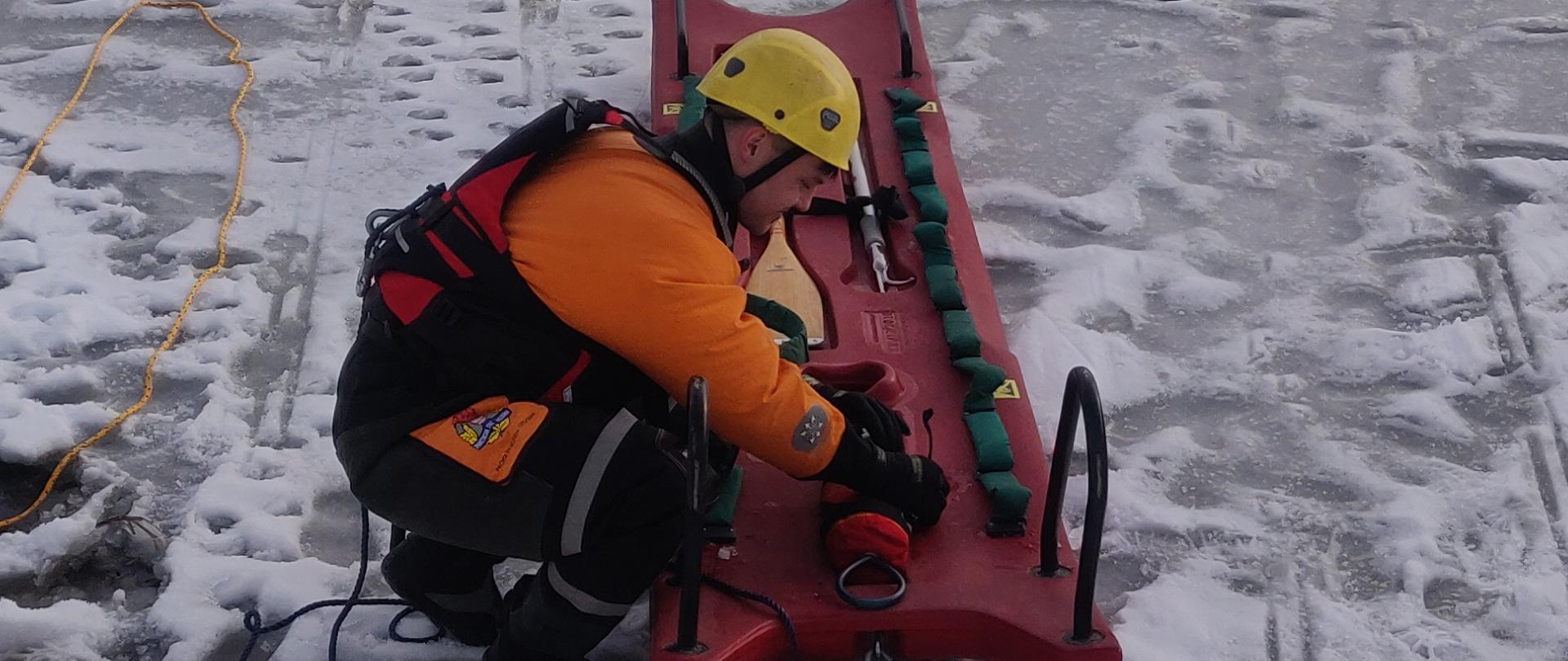 Na zdjęciu strażak przygotowuje sprzęt - sanie lodowe