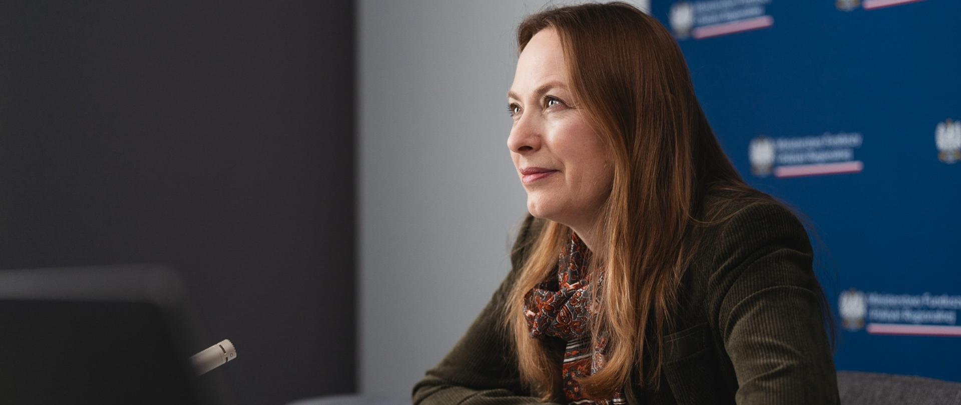 Minister Katarzyna Pełczyńska-Nałęcz siedzi przy stole z prawej strony i patrzy przed siebie. 