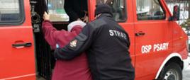 Strażak pomagający starszej kobiecie zając miejsce w samochodzie, który przewiezie ją do punktu szczepień
