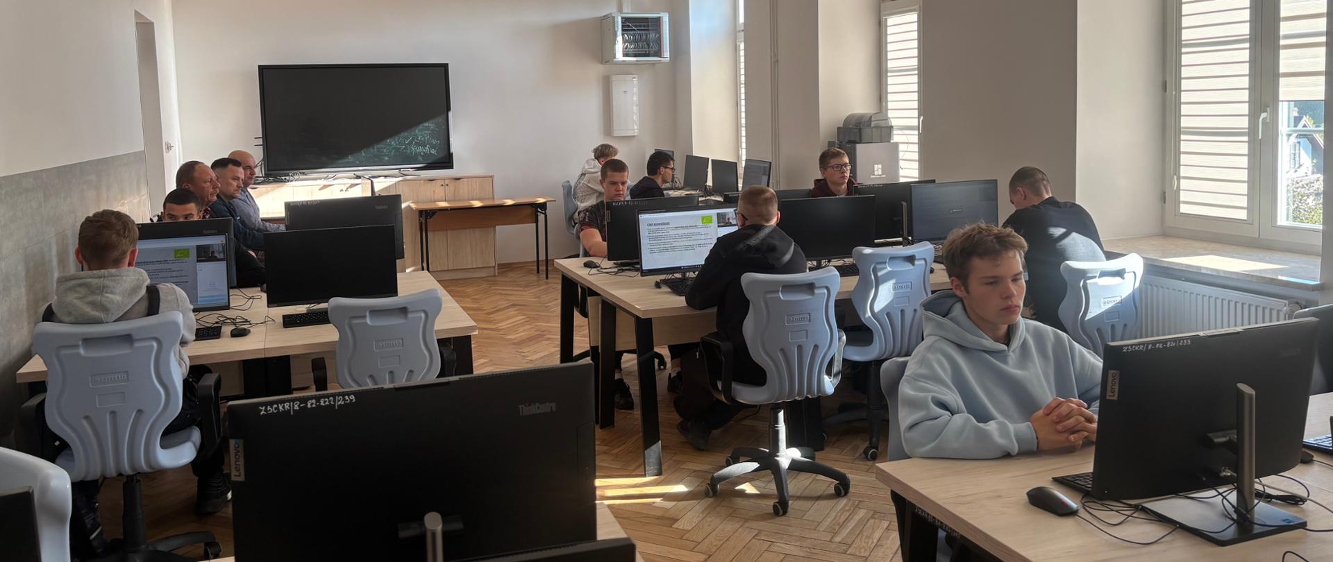 Uczniowie w pracowni czekają rozpoczęcie konkursu w tle po lewej stronie siedzą Panowie z komisji 
