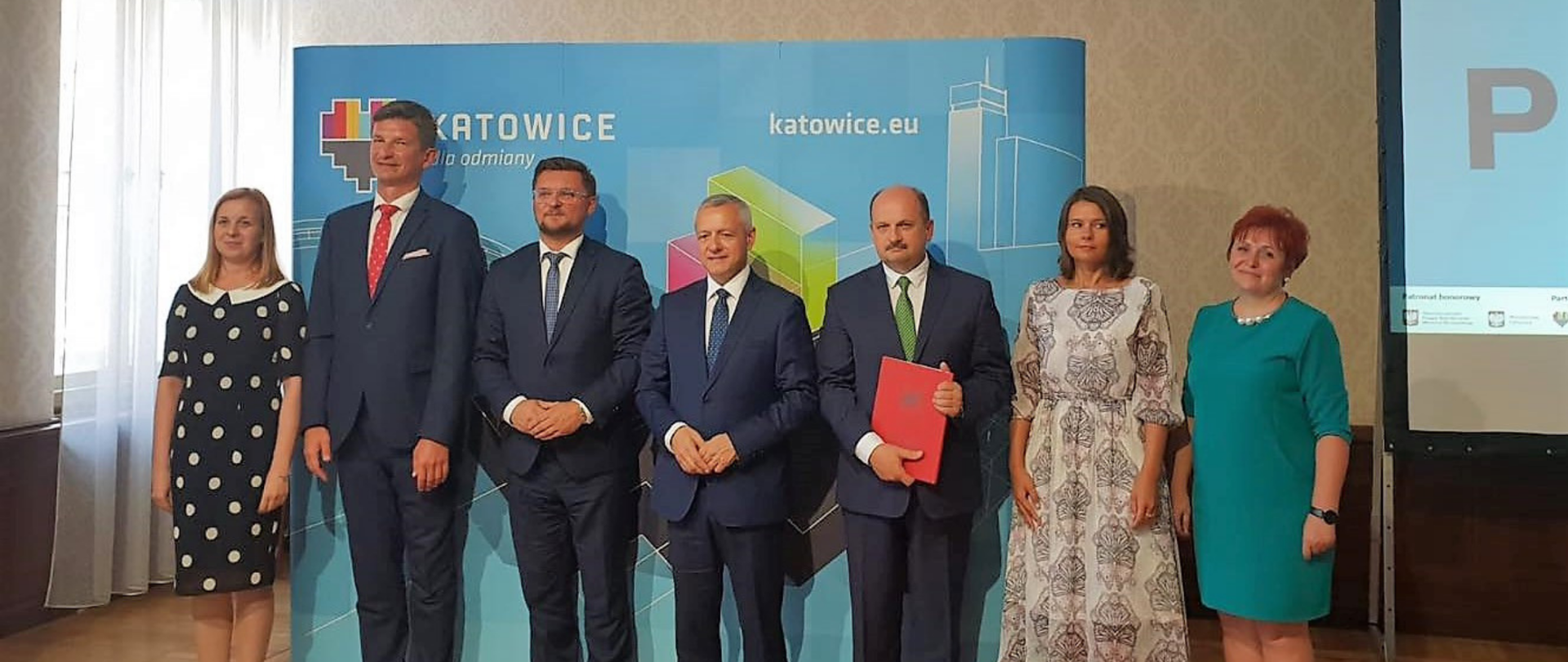 Osiem osób pozuje do wspólnego zdjęcia, na tle ścianki z logotypami Katowic